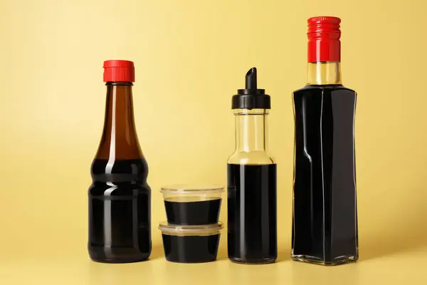 Bottles with soy sauce on yellow background