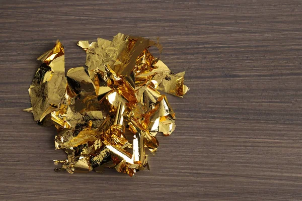 Pieces of edible gold leaf on wooden table, top view. Space for text