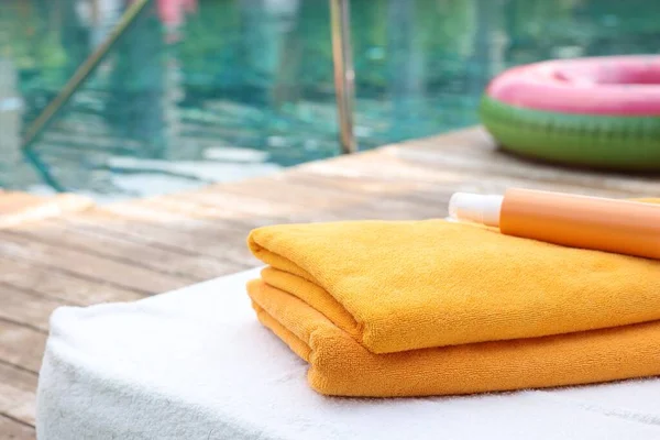 Beach towels and sunscreen on sun lounger near outdoor swimming pool at luxury resort, selective focus. Space for text