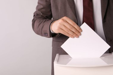 Adam oyunu açık gri arka planda oy sandığına koyuyor, yakın plan. Metin için boşluk