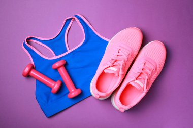 Şık spor kıyafetleri ve mor arka planda dambıllar düz yatıyordu.
