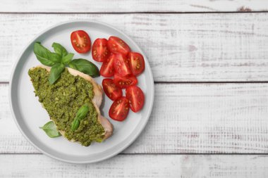 Pesto soslu leziz tavuk göğsü, beyaz ahşap masada domates ve fesleğen, üst manzara. Metin için boşluk