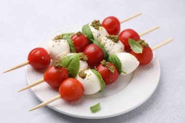 Domatesli şişler, mozarella topları, fesleğen ve pesto sosu beyaz masada, yakın plan.