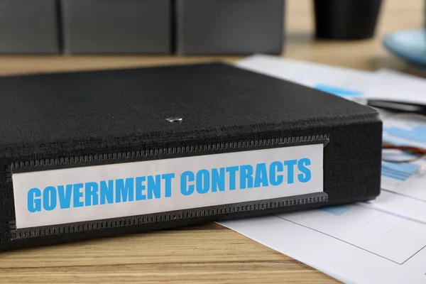 Black folder with Government Contracts label on desk in office, closeup
