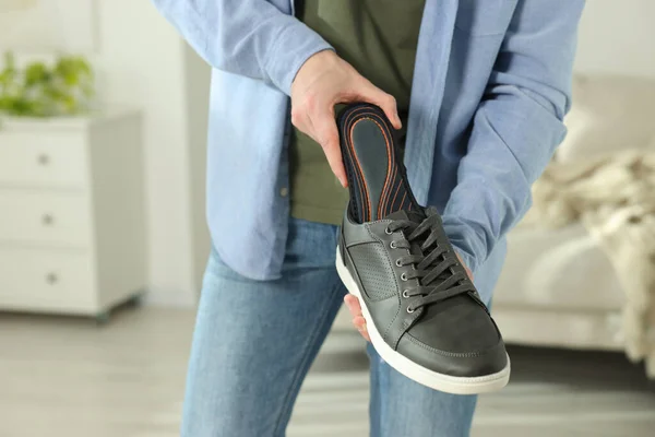 Man putting orthopedic insole into shoe indoors, closeup. Space for text