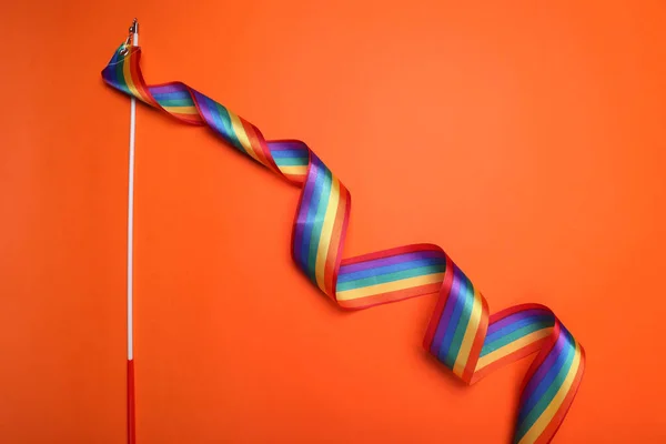 Stick with rainbow ribbon on orange background, top view. LGBT pride