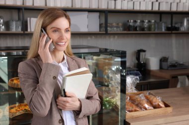 Pastanede telefonla konuşan defterli ve kalemli mutlu bir işletme sahibi.