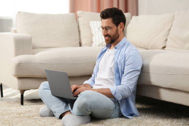 Evdeki kanepenin yanında dizüstü bilgisayar kullanan bir adam.