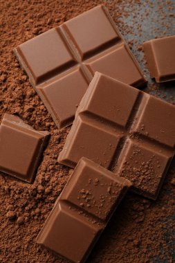 Lezzetli sütlü çikolata ve kakao tozu gri masada, yakın plan.