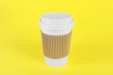 Sarı arka planda plastik kapaklı kağıt bardak. Kahve hazır.