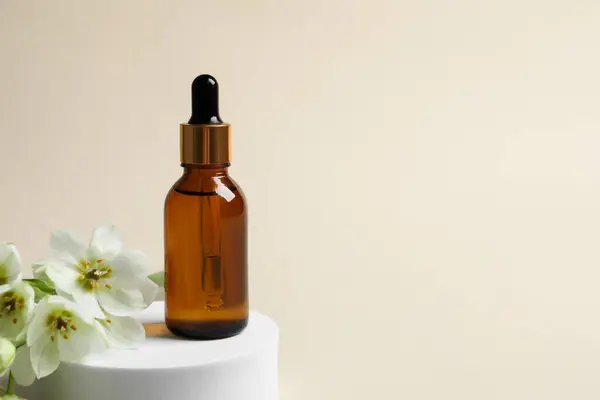 Bottle of cosmetic oil and flowers on beige background. Space for text