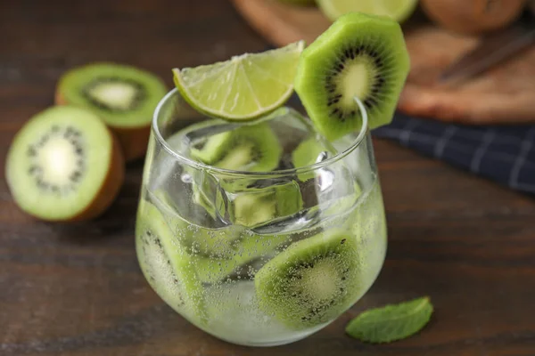 Glass of refreshing drink with cut kiwi on wooden table, closeup
