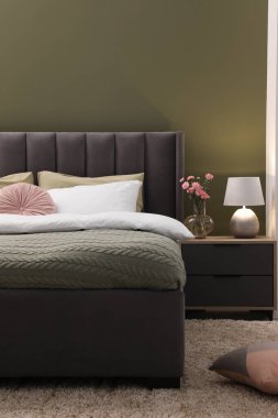 Büyük, rahat bir yatak, komodin, lamba ve şık bir odada güzel çiçekler. İç tasarım