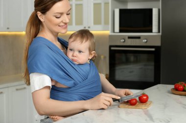 Anne mutfakta çocuğunu askıda tutarken domates kesiyor.