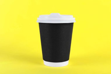 Sarı arka planda plastik kapaklı siyah kağıt bardak. Kahve hazır.