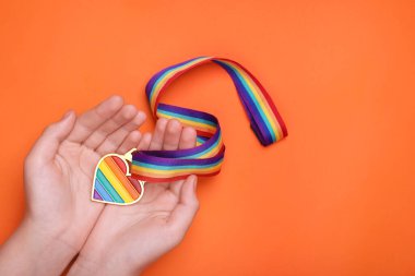 Turuncu arka planda kalp şeklinde kolyesi olan gökkuşağı kurdelesi tutan kadın, yazı için üst görüş ve boşluk. LGBT gururu