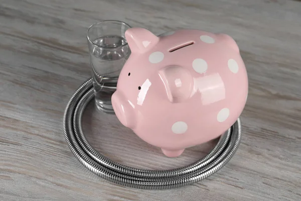 Water scarcity concept. Piggy bank, shower hose and glass of drink on wooden table