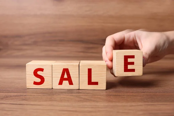 Woman making word Sale with cubes on wooden table, closeup