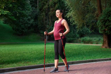 Hamile kadın dışarıda sırıklarla yürüme alıştırması yapıyor.