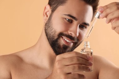 Elinde bej arka planda kozmetik serumu olan yakışıklı bir adam.
