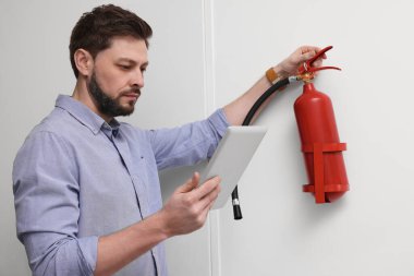 Tabletli adam yangın söndürücüyü içeride kontrol ediyor.