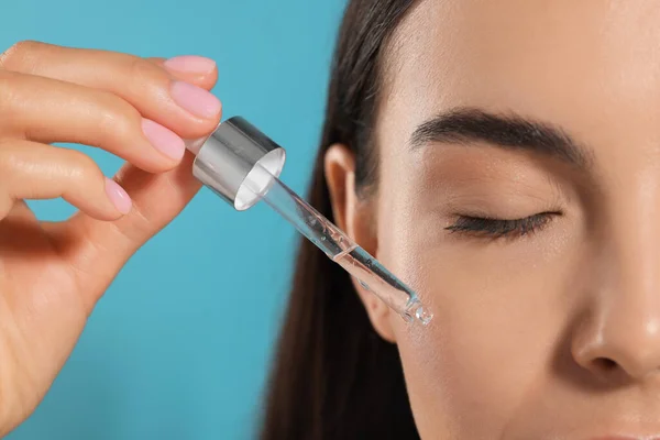 Young Woman Applying Serum Her Face Light Blue Background Closeup — Stock Photo, Image