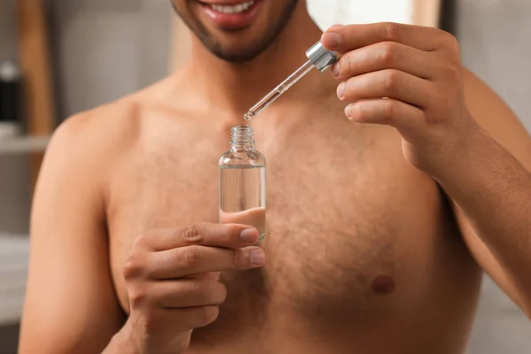 Man with cosmetic serum in hands in bathroom, closeup