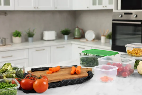 Containers with different fresh products, board and knife on white marble table in kitchen, space for text. Food storage