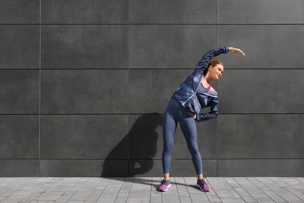 stock image Beautiful woman in gym clothes doing exercises on street, space for text