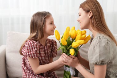 Kızı evde bir buket sarı laleyle annemi tebrik ediyor.