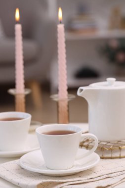Bir fincan çay, çaydanlık ve yanan mumlar.