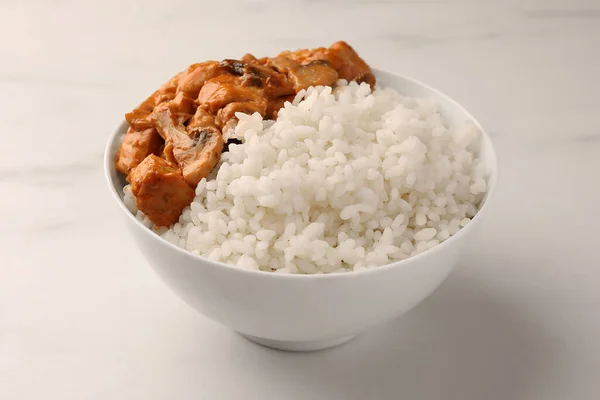 Bowl of delicious rice with meat and mushrooms on white marble table