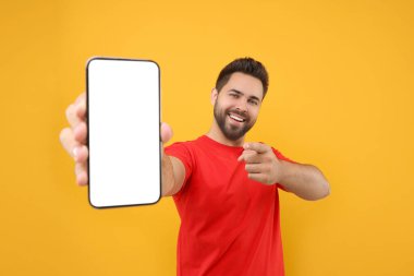 Genç adam elinde akıllı telefonu gösteriyor ve sarı arka planda onu işaret ediyor.