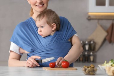 Anne çocuğunu askıda tutarken domates keser (bebek taşıyıcısı)