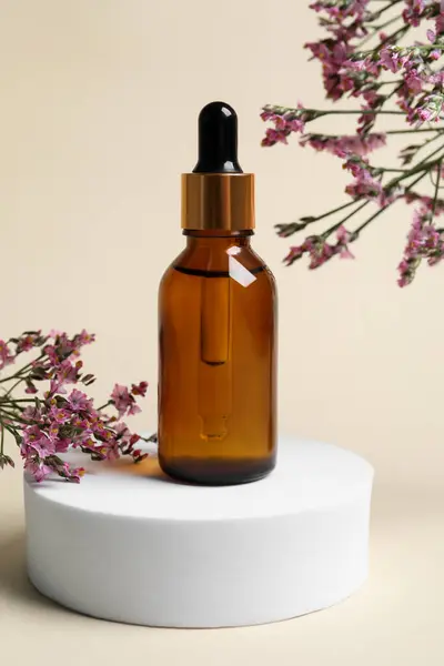 Bottle of cosmetic oil and flowers on beige background, closeup