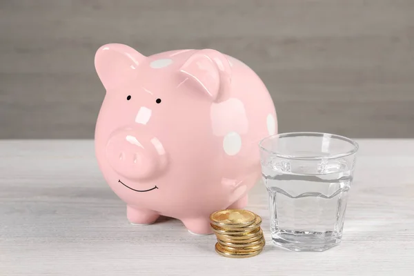 Water scarcity concept. Piggy bank, coins and glass of drink on white wooden table