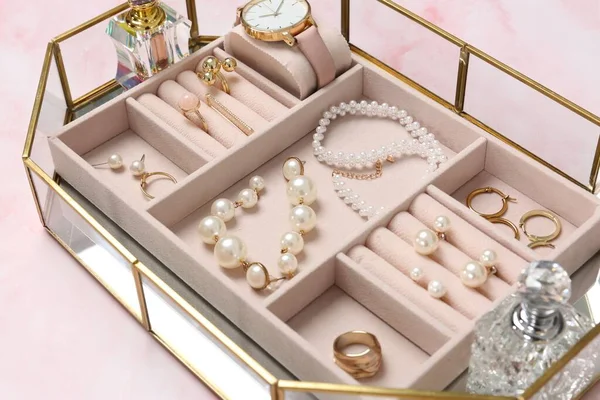 Jewelry box with many different accessories and perfumes on pink marble table, closeup