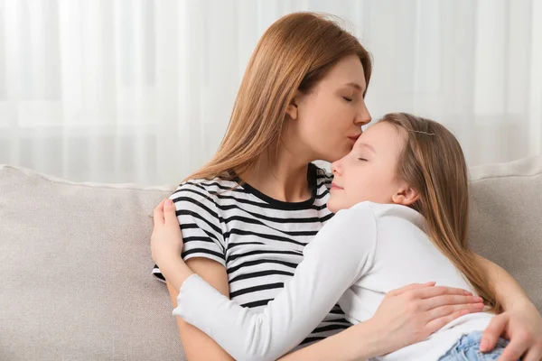 Mother kissing her cute daughter on sofa at home