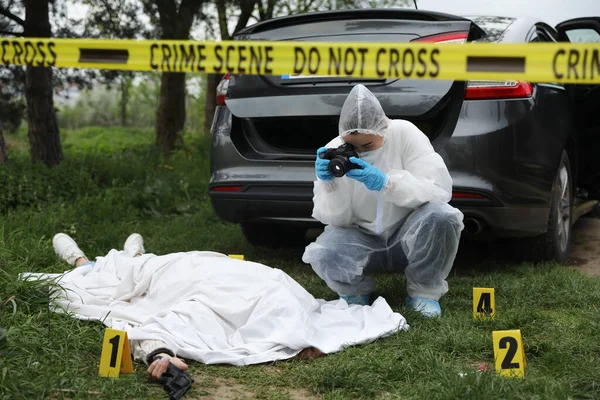 Criminologist taking photo of dead body at crime scene outdoors