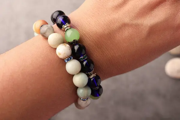 Woman wearing beautiful bracelets with gemstones on blurred background, closeup