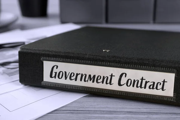 Black folder with Government Contract label on desk in office, closeup