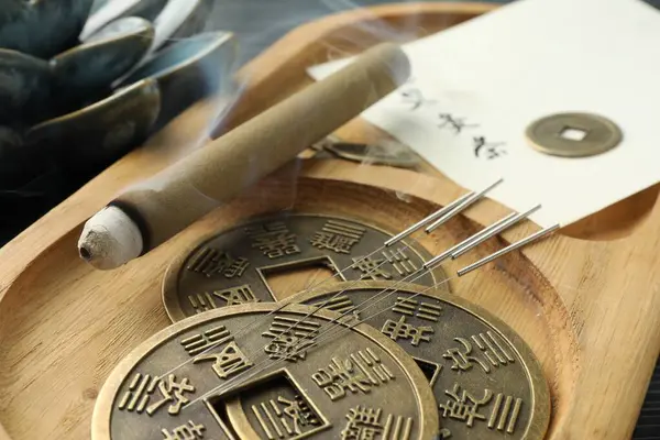 Acupuncture needles, moxa stick and antique Chinese coins on wooden tray, closeup