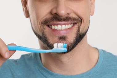 Beyaz arka planda plastik diş fırçasıyla dişlerini fırçalayan adam.