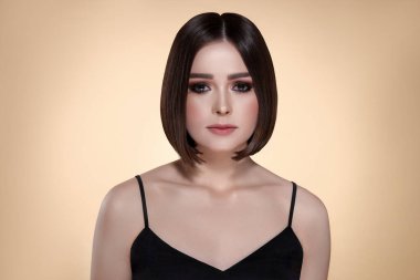 Bej arka planda kahverengi saçlı güzel bir genç kadının portresi.