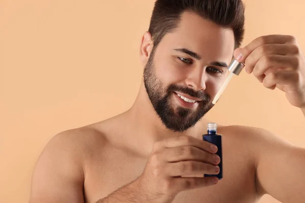 Handsome man with cosmetic serum in hands on beige background