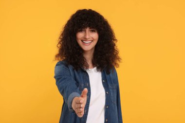Mutlu genç kadın karşılıyor ve sarı arka planda el sıkışmayı teklif ediyor.