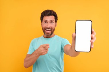 Yakışıklı bir adam elinde akıllı telefon gösteriyor ve onu sarı arka planda işaret ediyor.