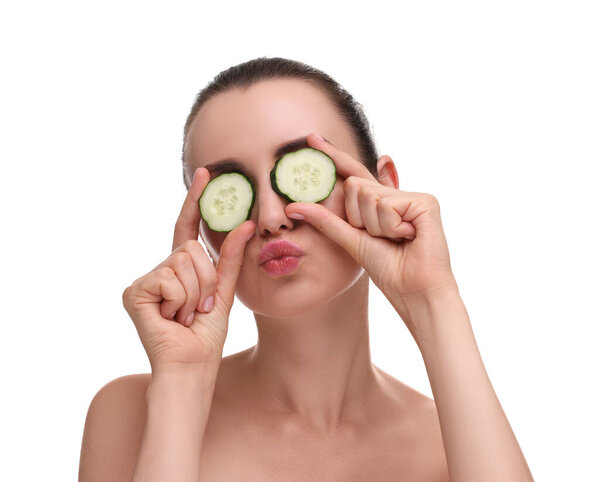 Beautiful woman covering eyes with pieces of cucumber and blowing kiss on white background