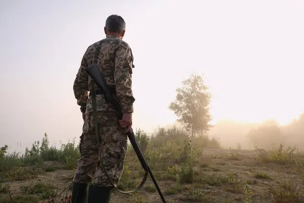 Man with hunting rifle wearing camouflage outdoors, back view. Space for text
