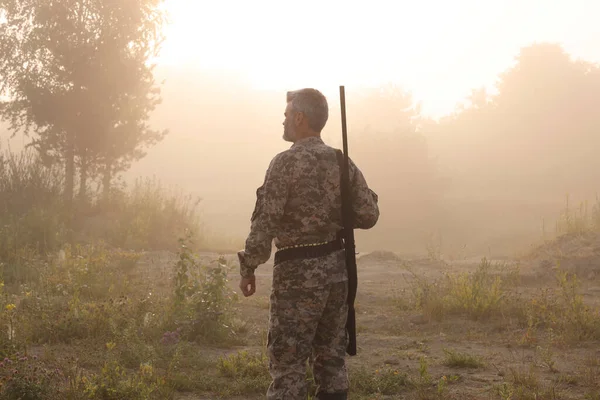 Man with hunting rifle wearing camouflage outdoors, back view